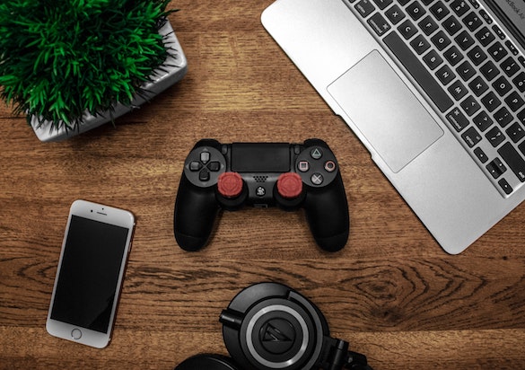 Gamepad, Notebook, Handy und Kopfhörer auf einer Tischoberfläche